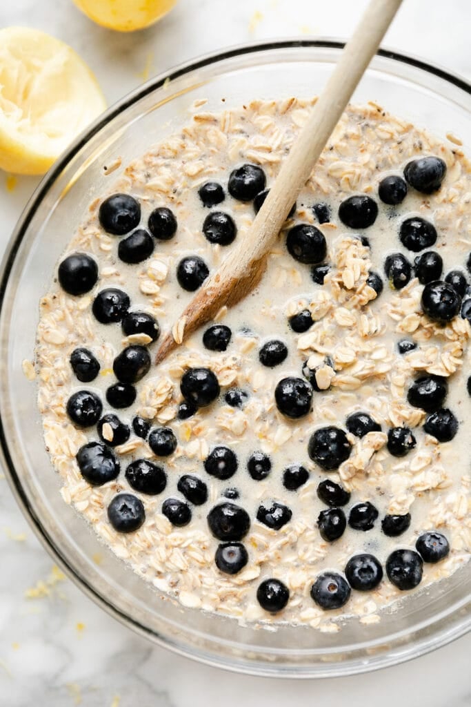 Close up view of a bowl of oatmeal with a wooden spoon stirring in fresh blueberries. 