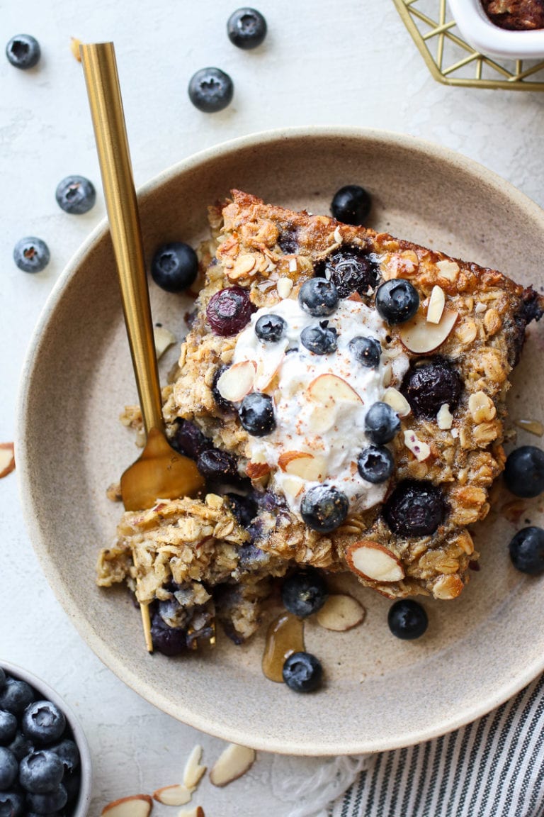 Overhead view of a piece of healthy blueberry baked oatmeal topped with whipped cream and almond slices. 