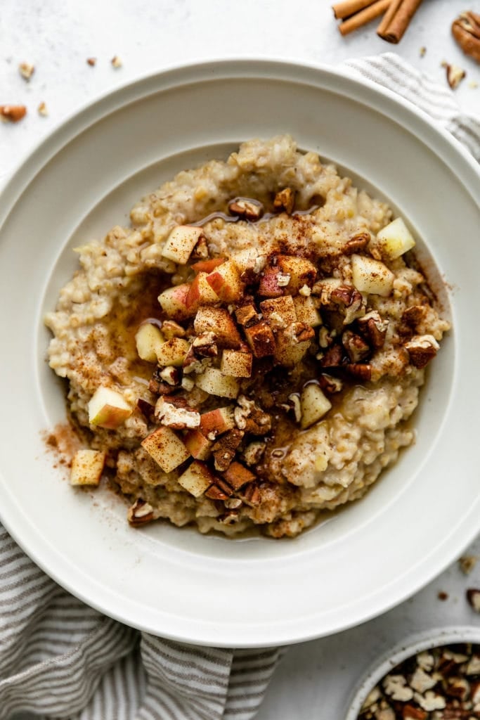 Overhead view of a bowl of oatmeal topped with apple chunks and sprinkled with cinnamon. 