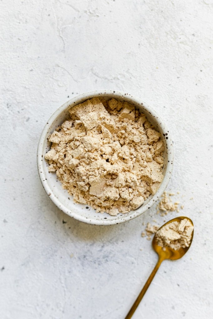 Close up view of protein powder in a white bowl with a gold spoon beside it. 